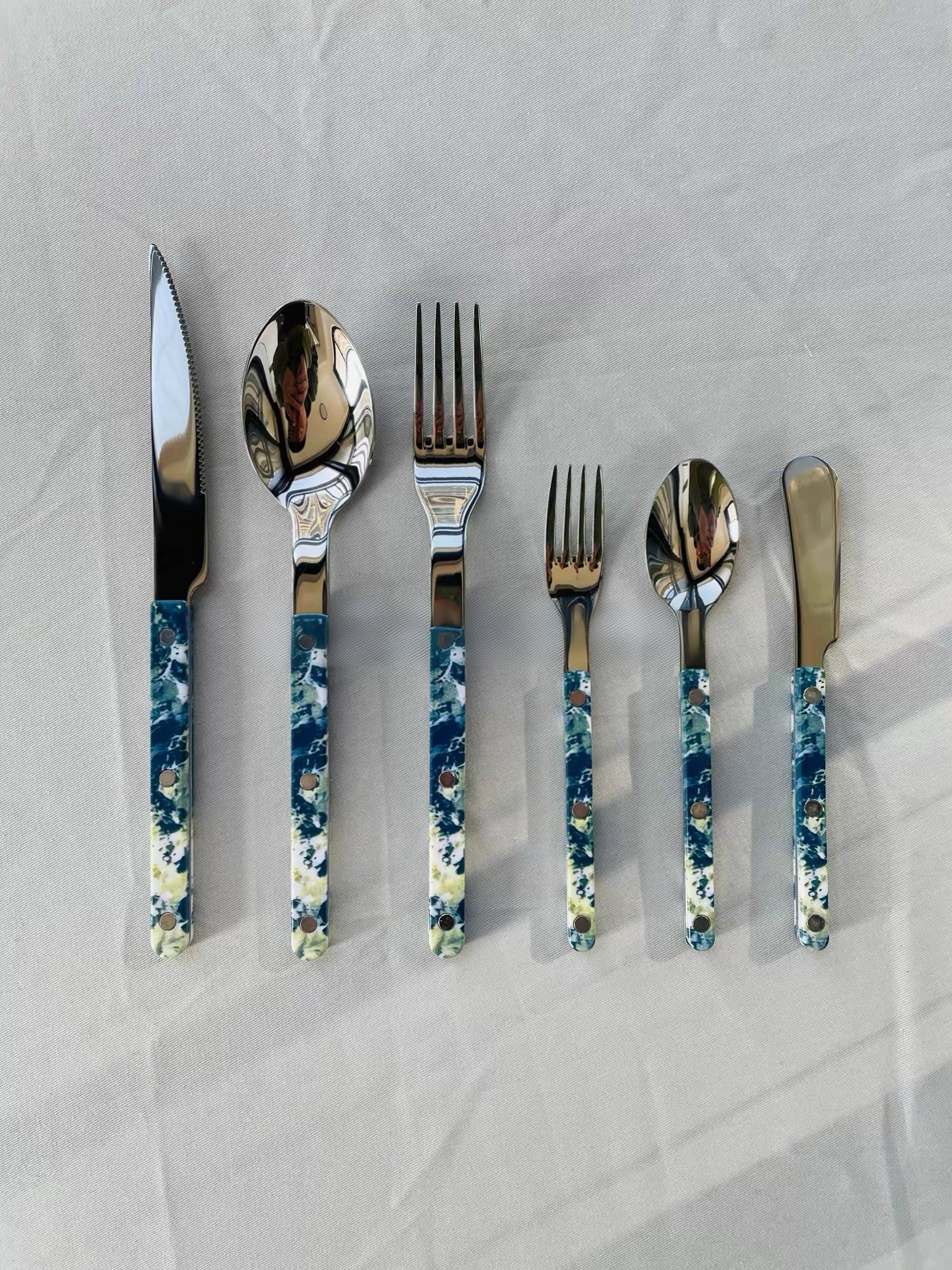 Set of silver cutlery with blue and white patterned handles on a light gray background