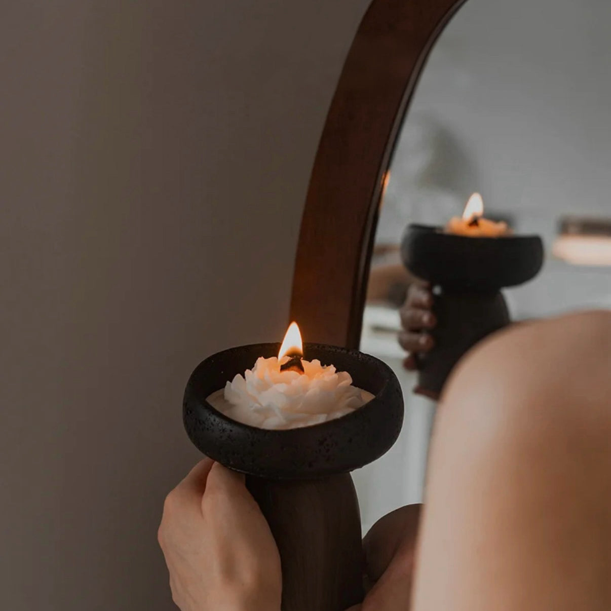 Person holding a lit candle in a decorative holder in front of a mirror.