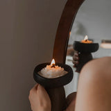 Person holding a lit candle in a decorative holder in front of a mirror.