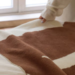 Brown and beige patterned blanket on a bed with a person partially visible.