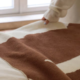Brown and beige patterned blanket on a bed with a person partially visible.
