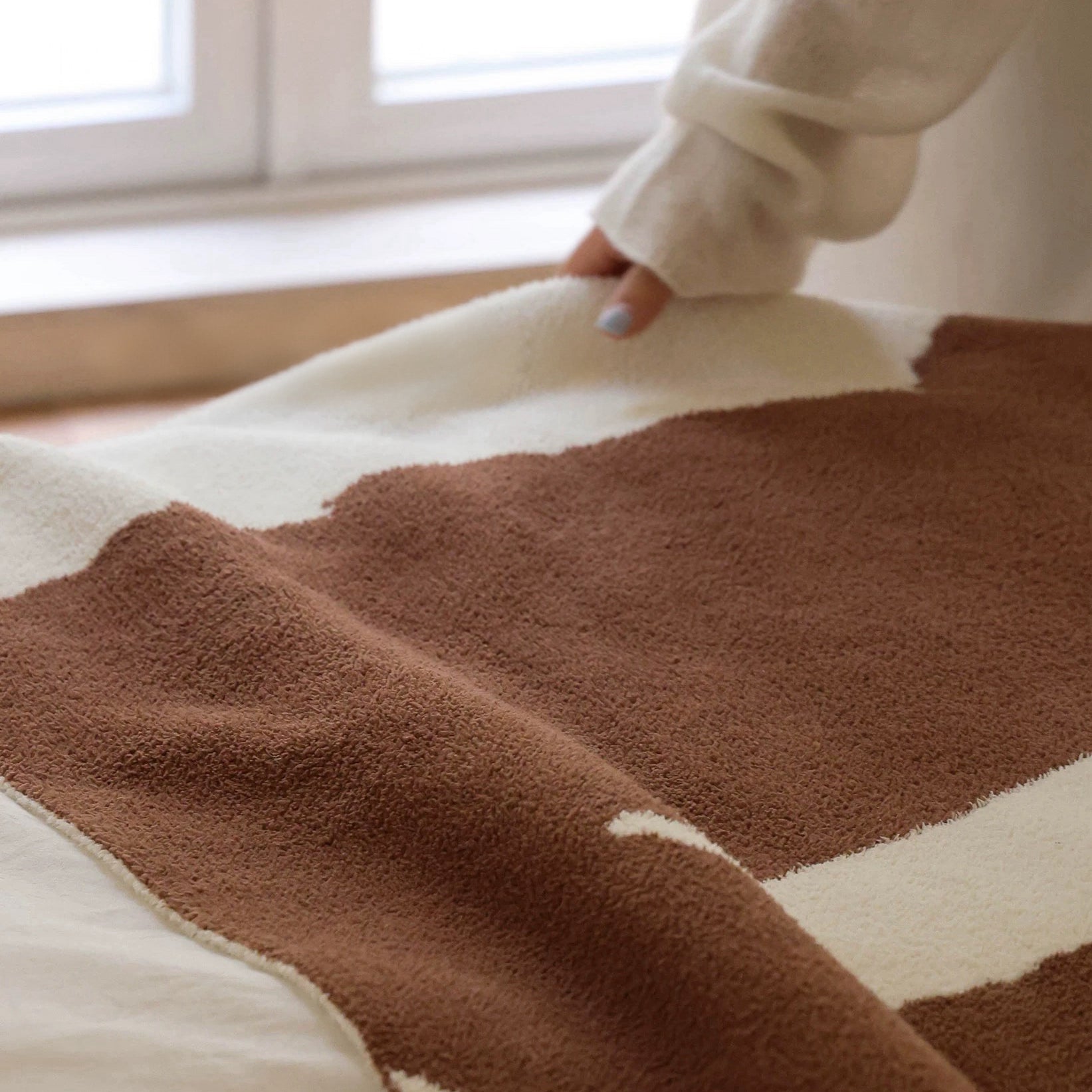 Brown and beige patterned blanket on a bed with a person partially visible.