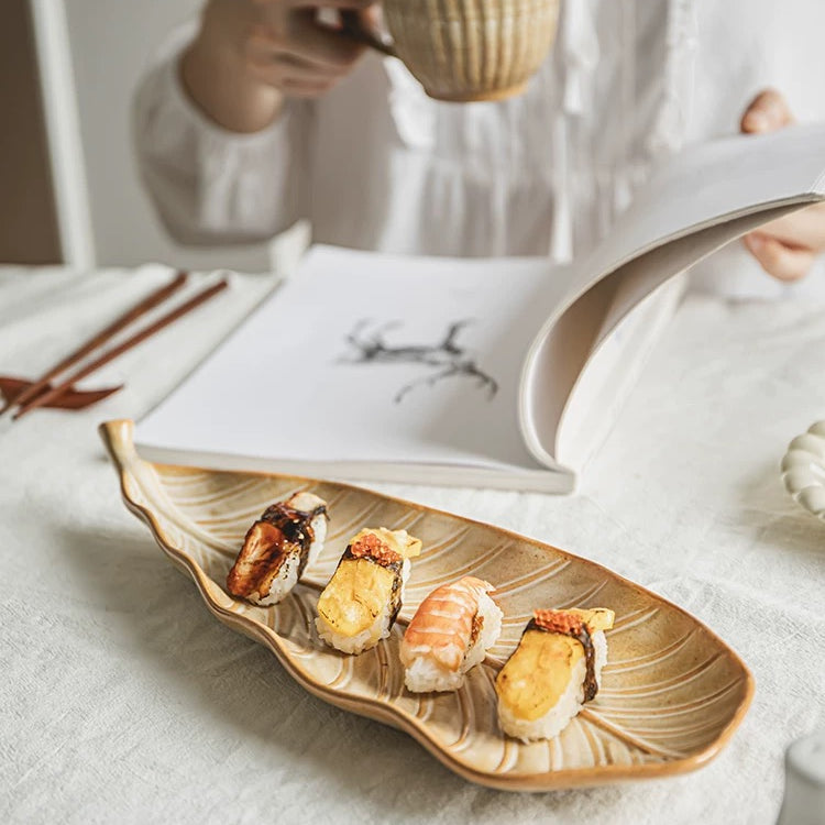 Person holding a cup with a leaf-shaped plate of sushi on a light surface