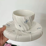 Ceramic cup and saucer with floral design held against a white background