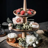 Three-tiered wooden serving tray with fruits, flowers, and a candle on a dark background