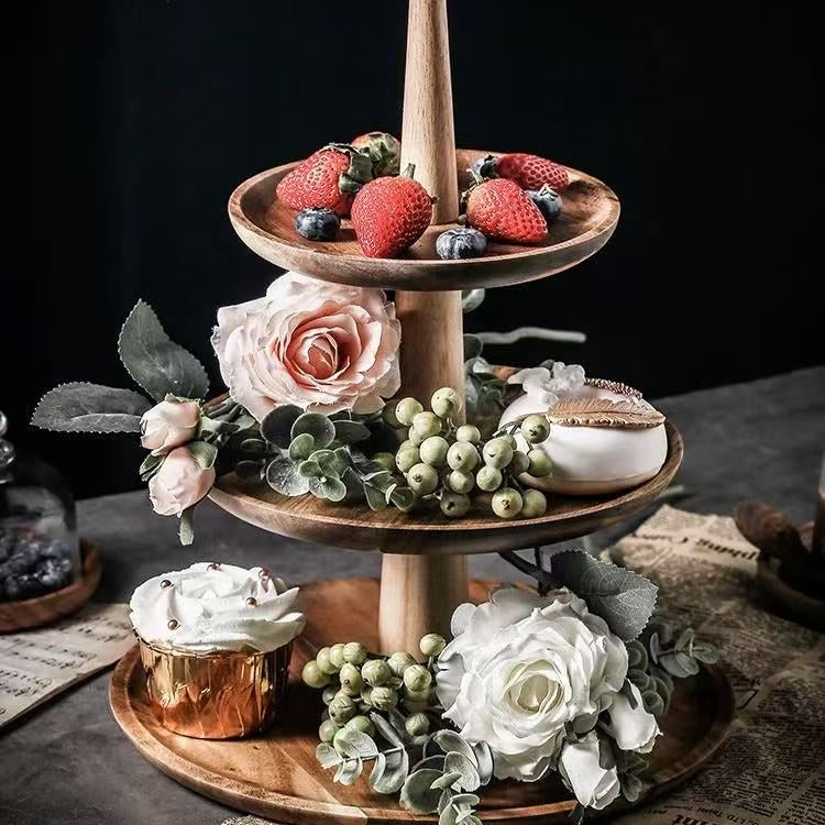 Three-tiered wooden serving tray with fruits, flowers, and a candle on a dark background