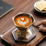 Cappuccino with latte art on a wooden tray, with a hand reaching towards it.