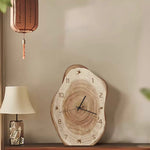 Wooden wall clock on a shelf with a lamp and decorative item in the background.