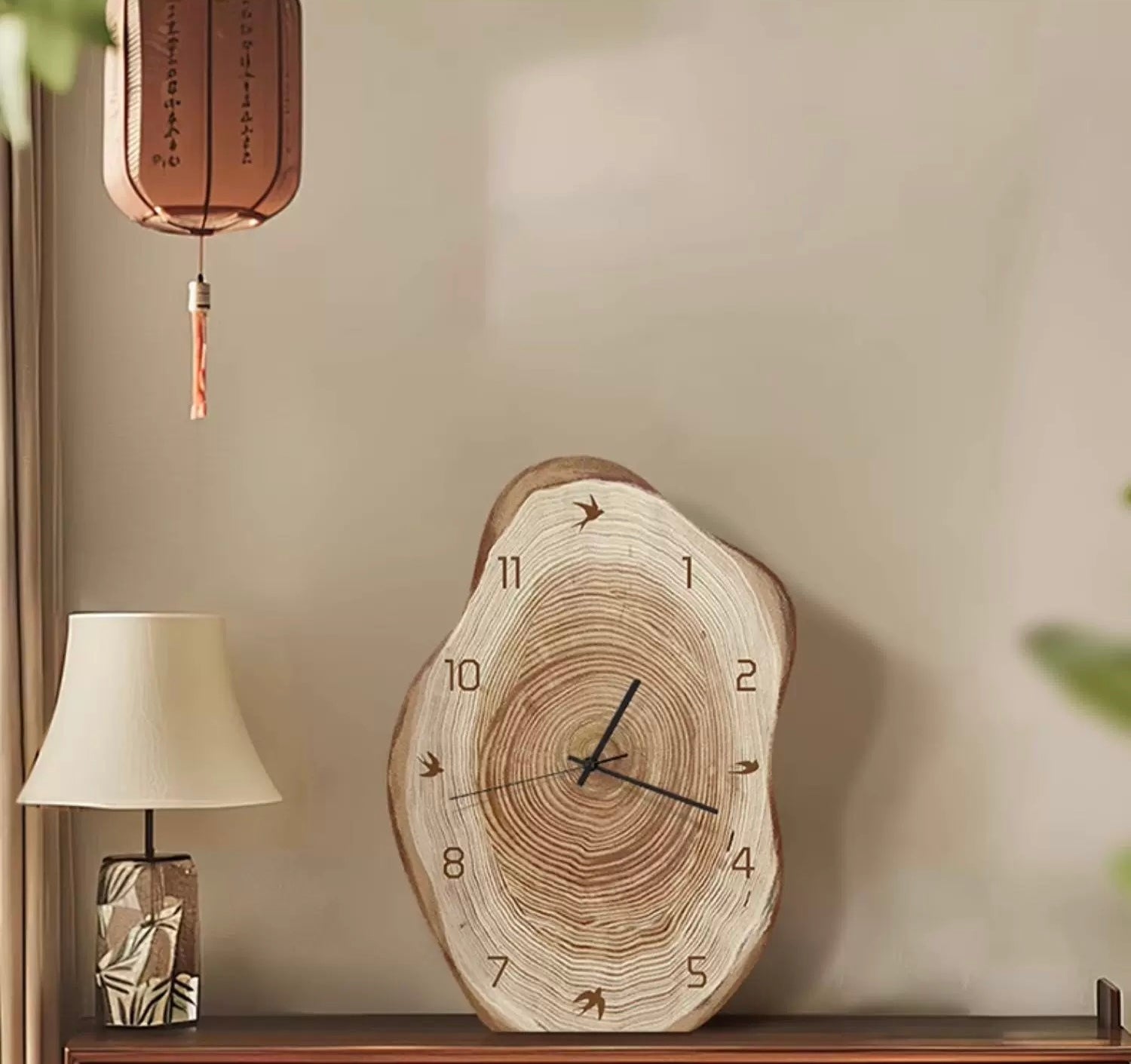 Wooden wall clock on a shelf with a lamp and decorative item in the background.
