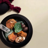 Black bowl with rocks, crystals, and a spoon on a beige background