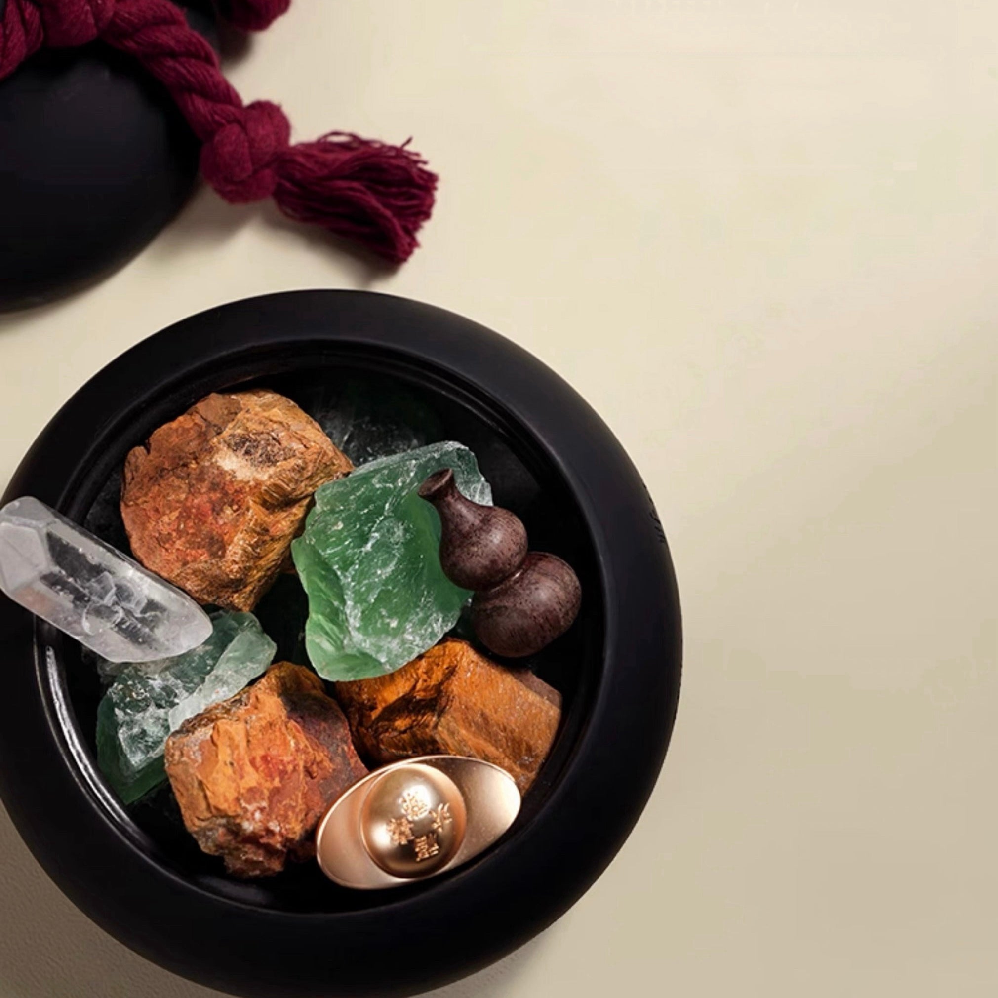 Black bowl with rocks, crystals, and a spoon on a beige background