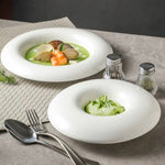 Two white bowls with green soup and garnishes on a gray surface with silverware and saltshakers.