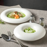 Two white bowls with green soup and garnishes on a gray surface with silverware and saltshakers.