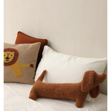 A brown dog-shaped cushion pillow on a bed, with other pillows and bedding in the background.