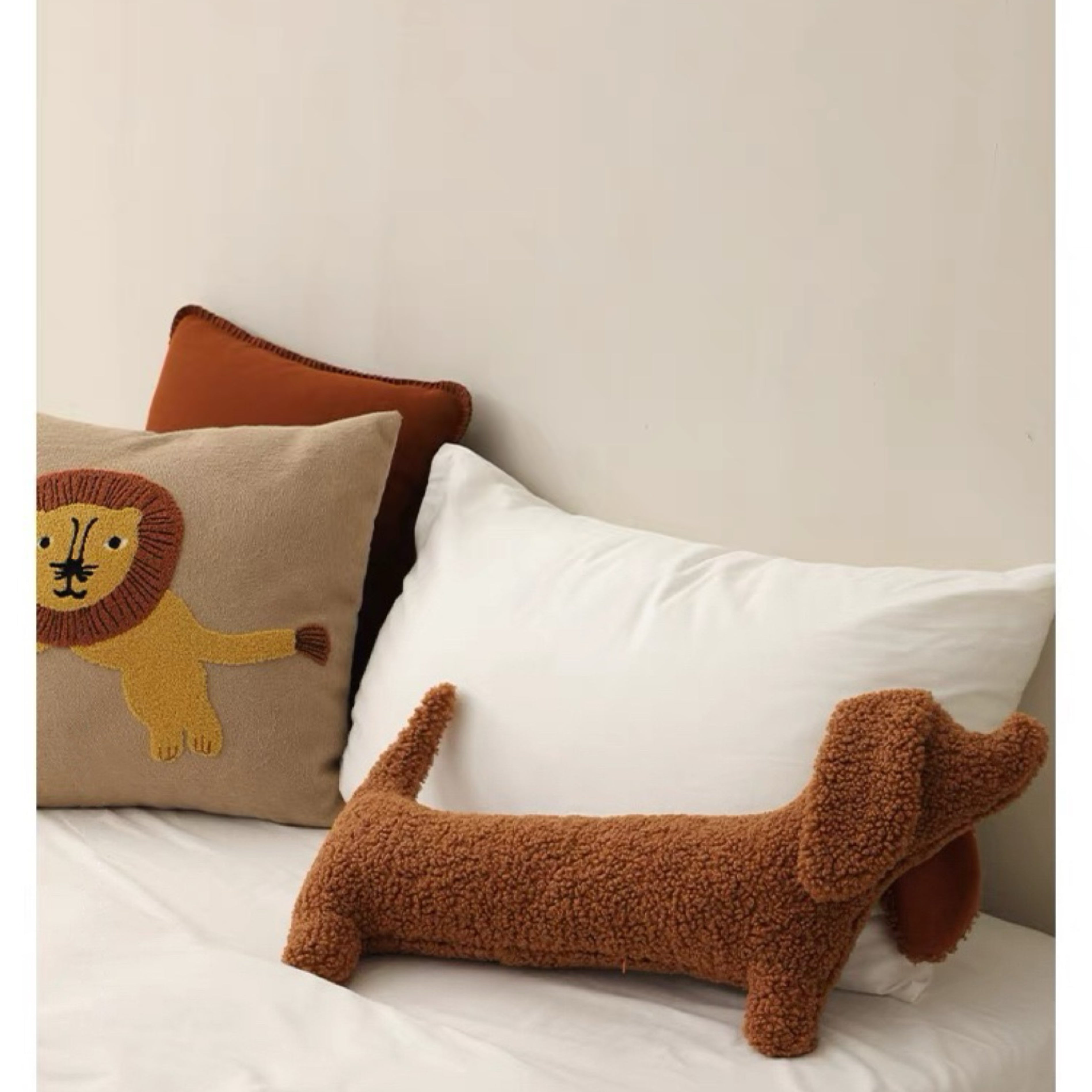 A brown dog-shaped cushion pillow on a bed, with other pillows and bedding in the background.