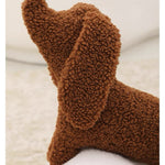 A brown dog-shaped cushion pillow on a bed, with other pillows and bedding in the background.