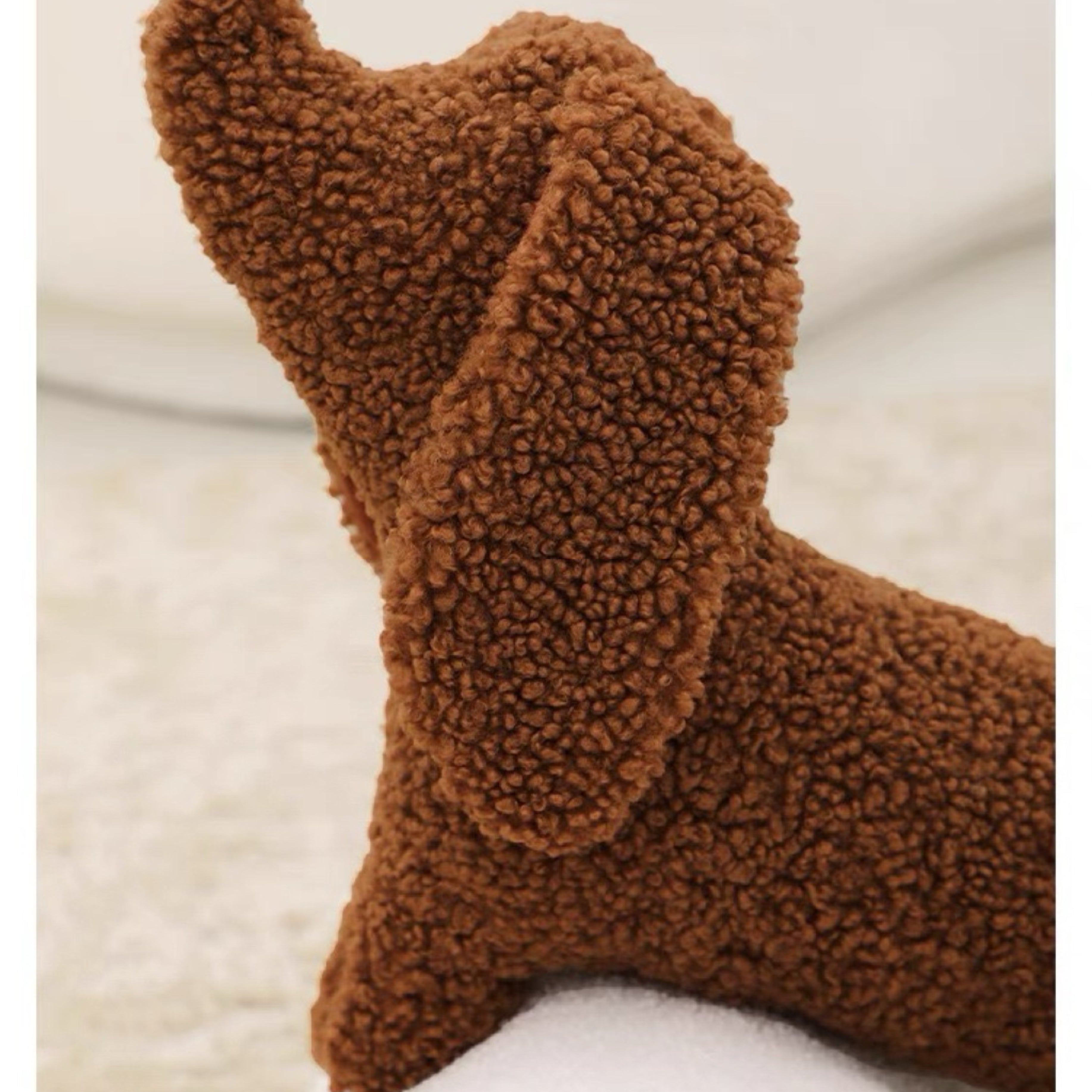 A brown dog-shaped cushion pillow on a bed, with other pillows and bedding in the background.