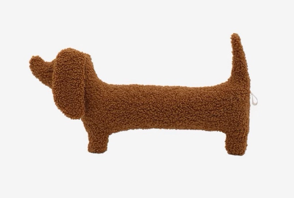 A brown dog-shaped cushion pillow on a bed, with other pillows and bedding in the background.
