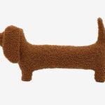 A brown dog-shaped cushion pillow on a bed, with other pillows and bedding in the background.