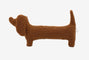 A brown dog-shaped cushion pillow on a bed, with other pillows and bedding in the background.