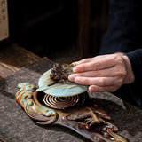 Hand interacting with an ornate metal object on a textured surface