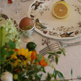 Table setting with floral arrangement, lemon, egg, and silverware on a decorative plate.