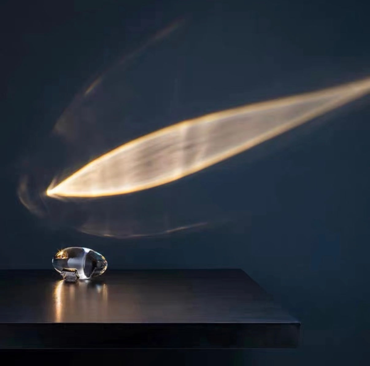 Crystal object on a dark surface with a light beam casting a shadow.