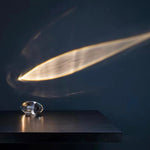 Crystal object on a dark surface with a light beam casting a shadow.