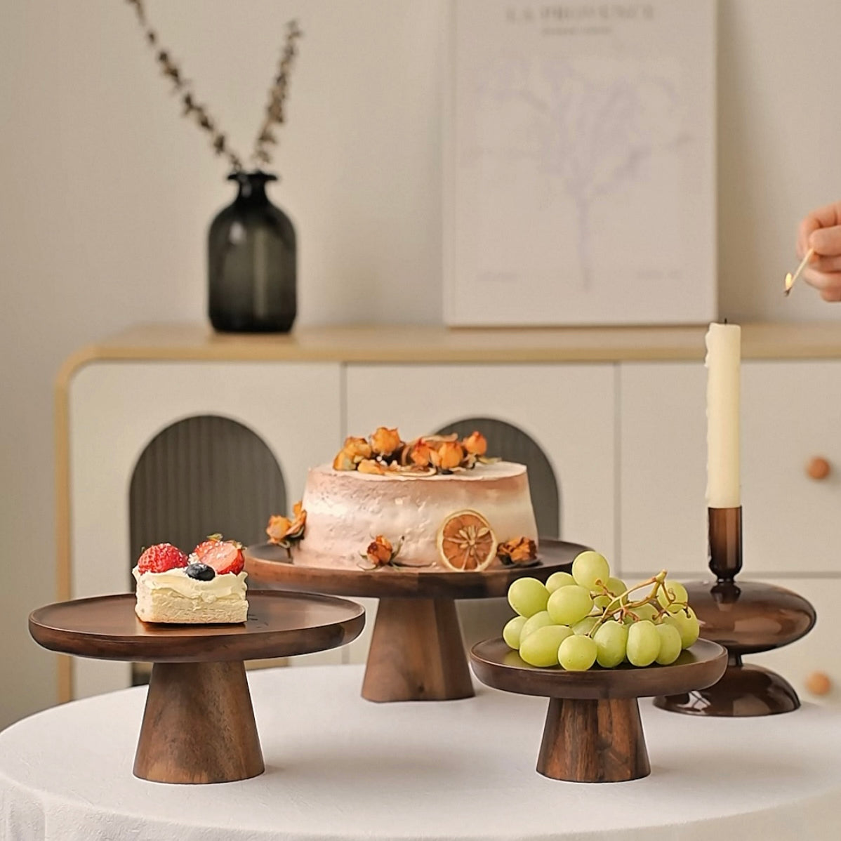 Wooden cake stands with small cakes and fruits on a table.