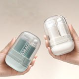 Two hands holding small cylindrical containers, one green and one white, against a beige background.