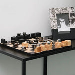 Modern chess set with black and wood pieces on a table against a plain wall.