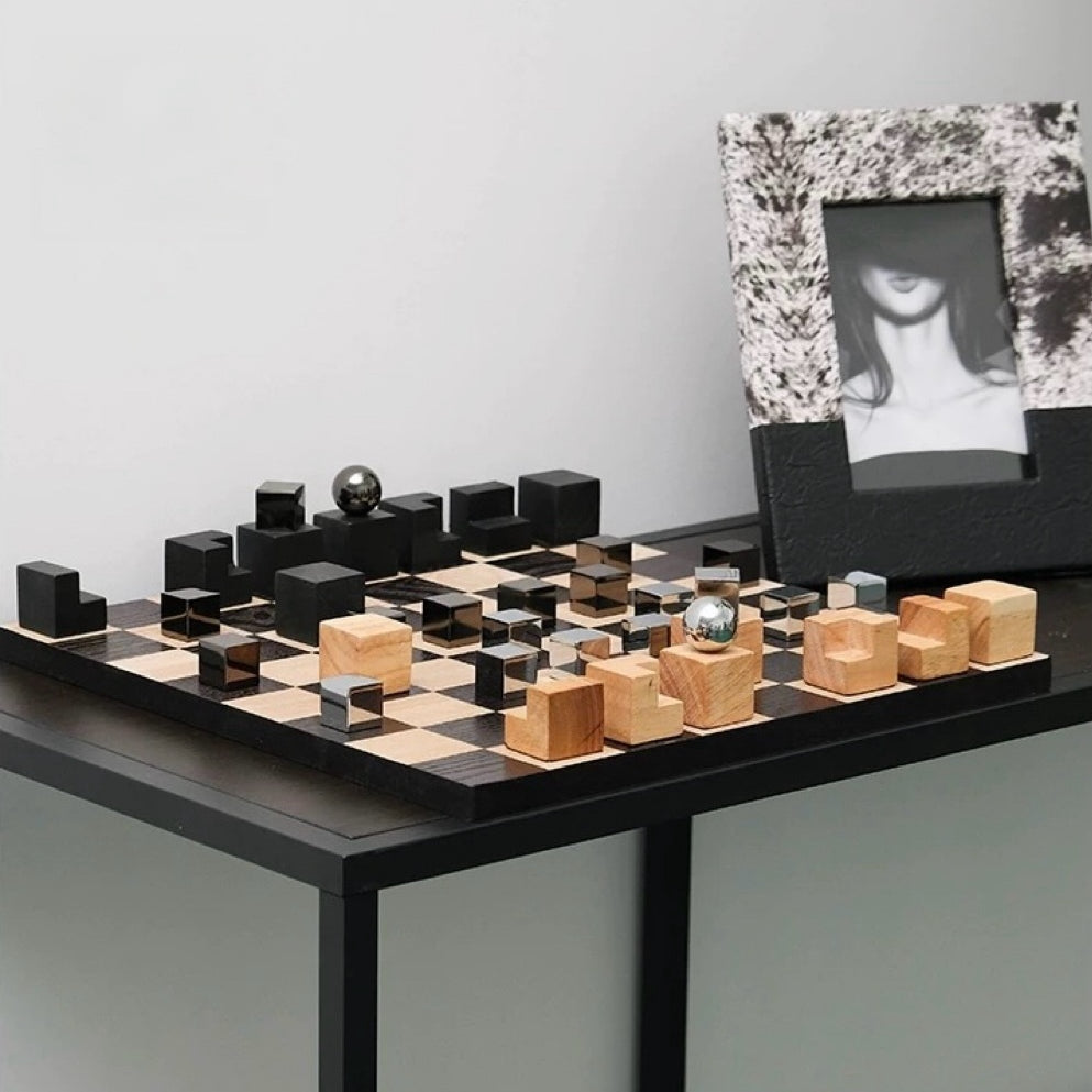 Modern chess set with black and wood pieces on a table against a plain wall.