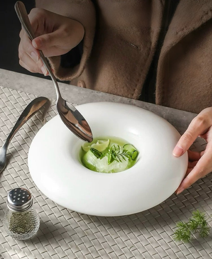 White bowl with green soup on a textured surface, person holding a spoon