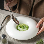 White bowl with green soup on a textured surface, person holding a spoon