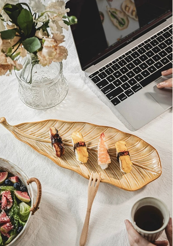 Laptop on a table with sushi, coffee, and flowers