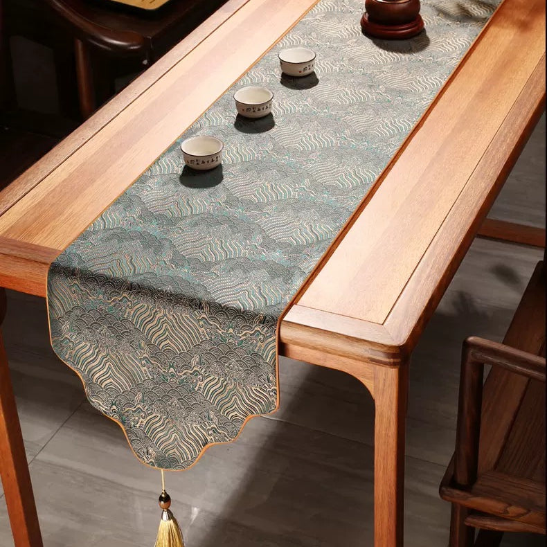 Wooden table with a decorative table runner and small cups on a wooden floor.