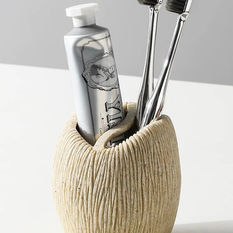 Beige ceramic holder with toothbrushes and a bottle on a white surface