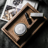 Wooden tray with cosmetic items including a compact mirror, lipstick, and small box on a dark fabric background.