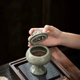 Person holding a ceramic incense burner on a wooden table with a dark background