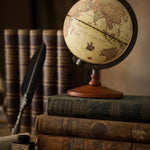 Vintage globe on a stack of old books with a feather quill and inkwell in the background.