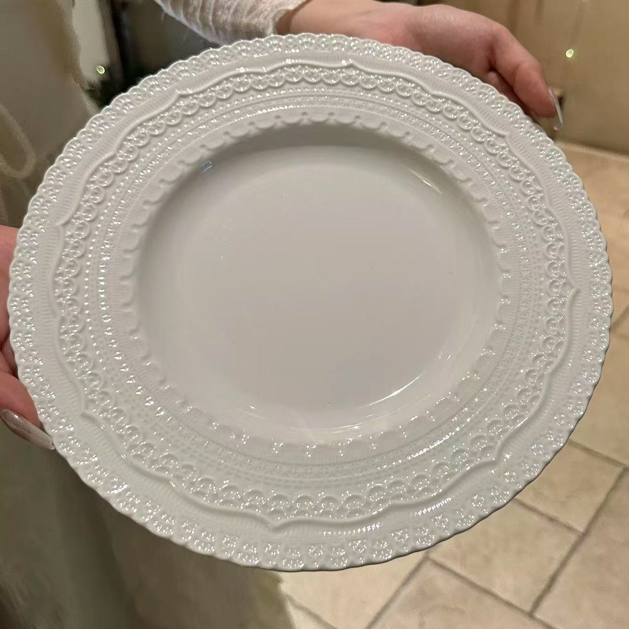 White decorative plate held by a person on a tiled floor.