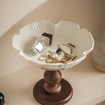 White jewelry dish with wooden base holding jewelry on a neutral background