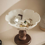 White jewelry dish with wooden base holding jewelry on a neutral background