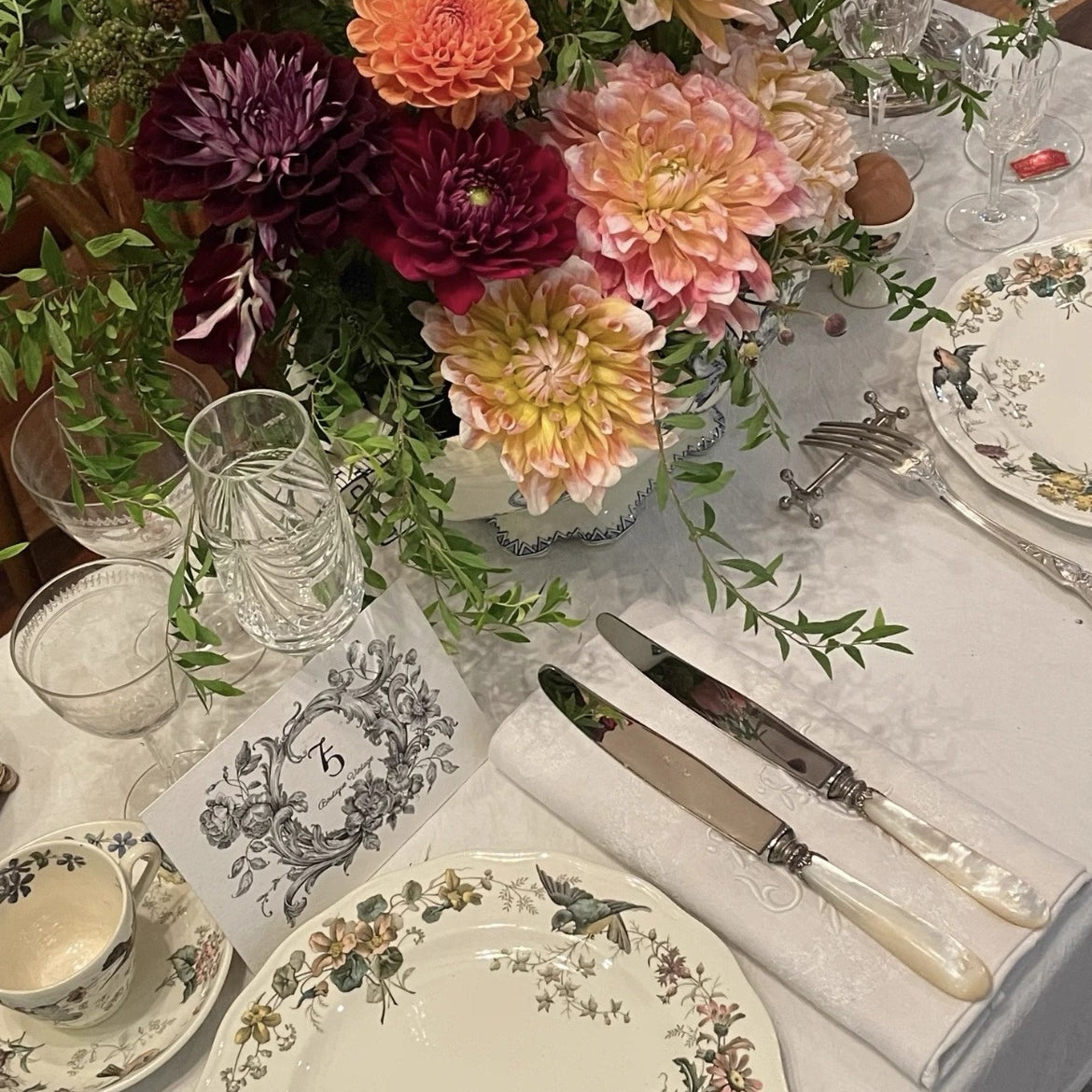 Elegant table setting with floral centerpiece, plates, and cutlery on a white tablecloth.