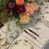 Elegant table setting with floral centerpiece, plates, and cutlery on a white tablecloth.