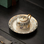 Decorative teapot and saucer set with intricate designs on a dark surface