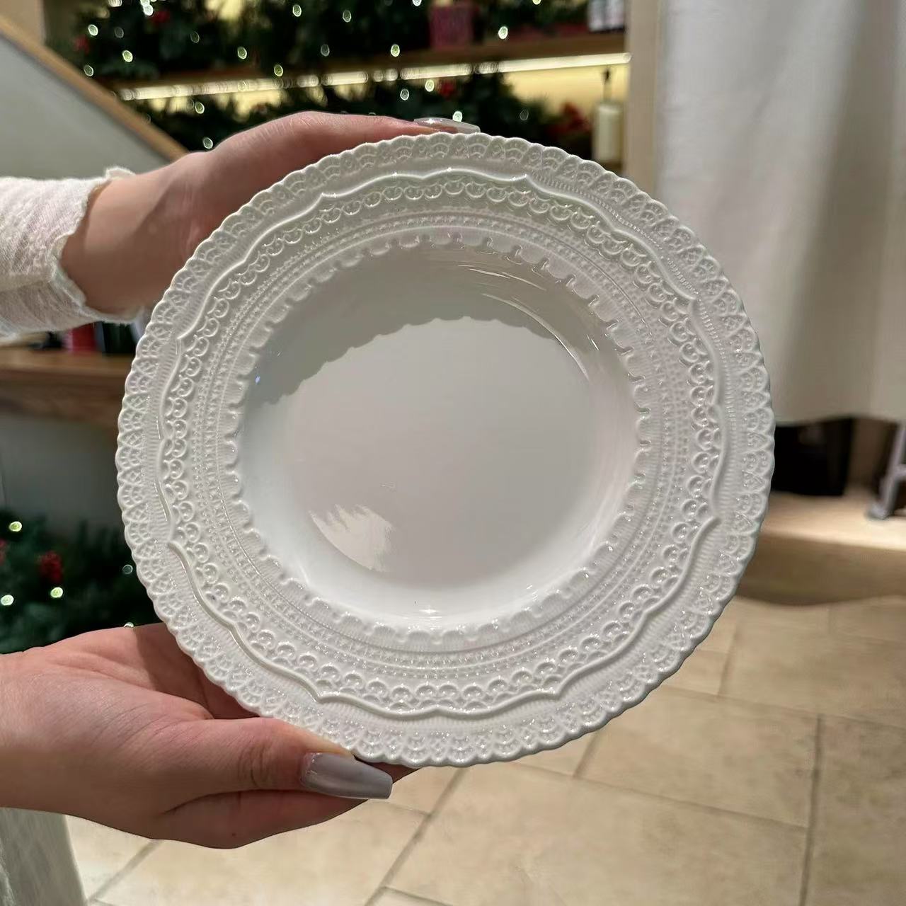 White decorative plate held by a person in a home setting with blurred background