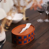 Tissue box with checkered design on a wooden table with wine glasses and decorative elements.