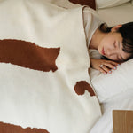 Person lying on a bed with a cow print blanket