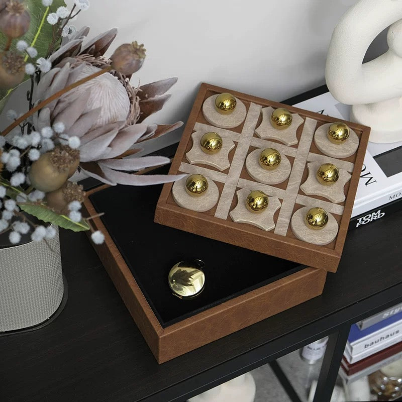 Wooden tic-tac-toe game set with gold pieces on a table with decorative items.
